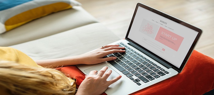 A woman is designing a website on a laptop that is kept on her lap